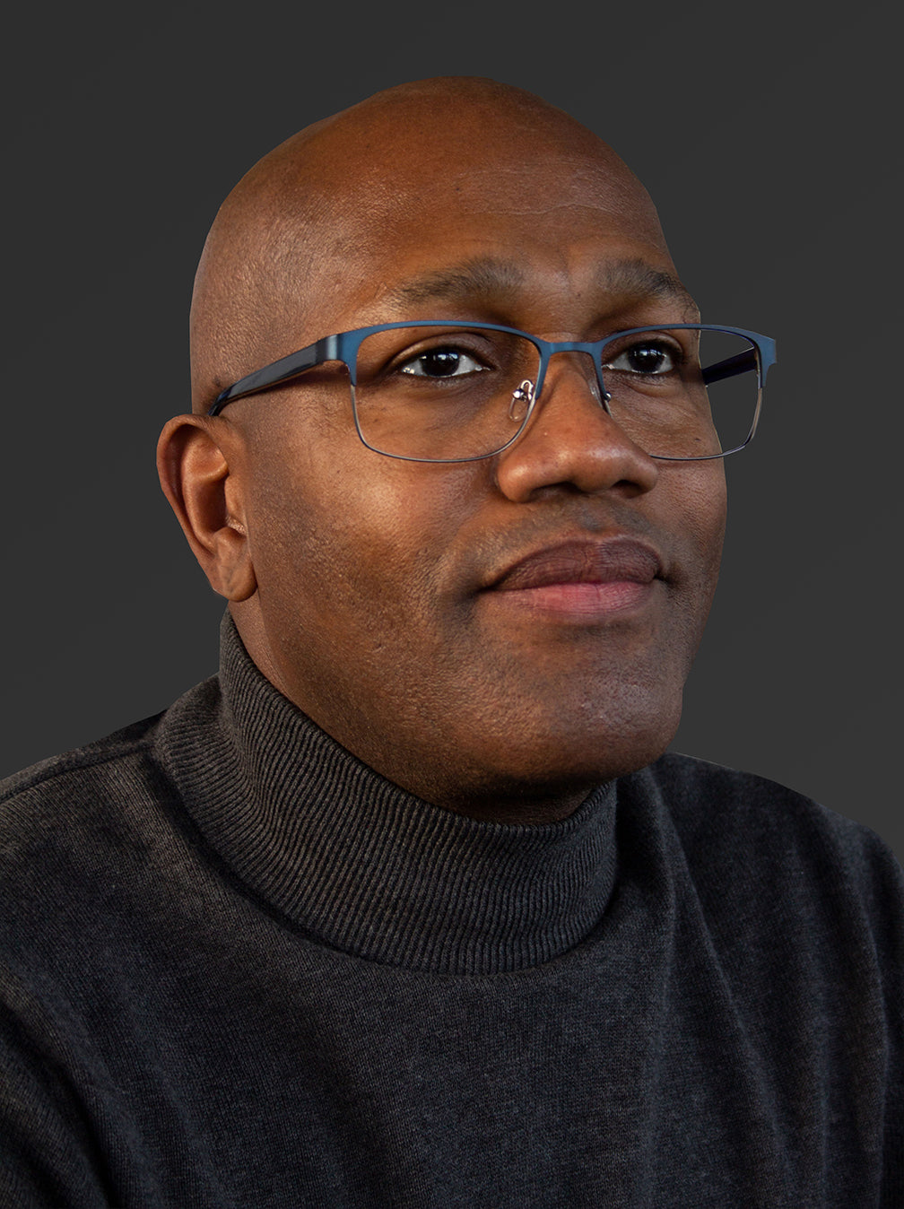 Man wearing glasses and a dark sweater against a gray background