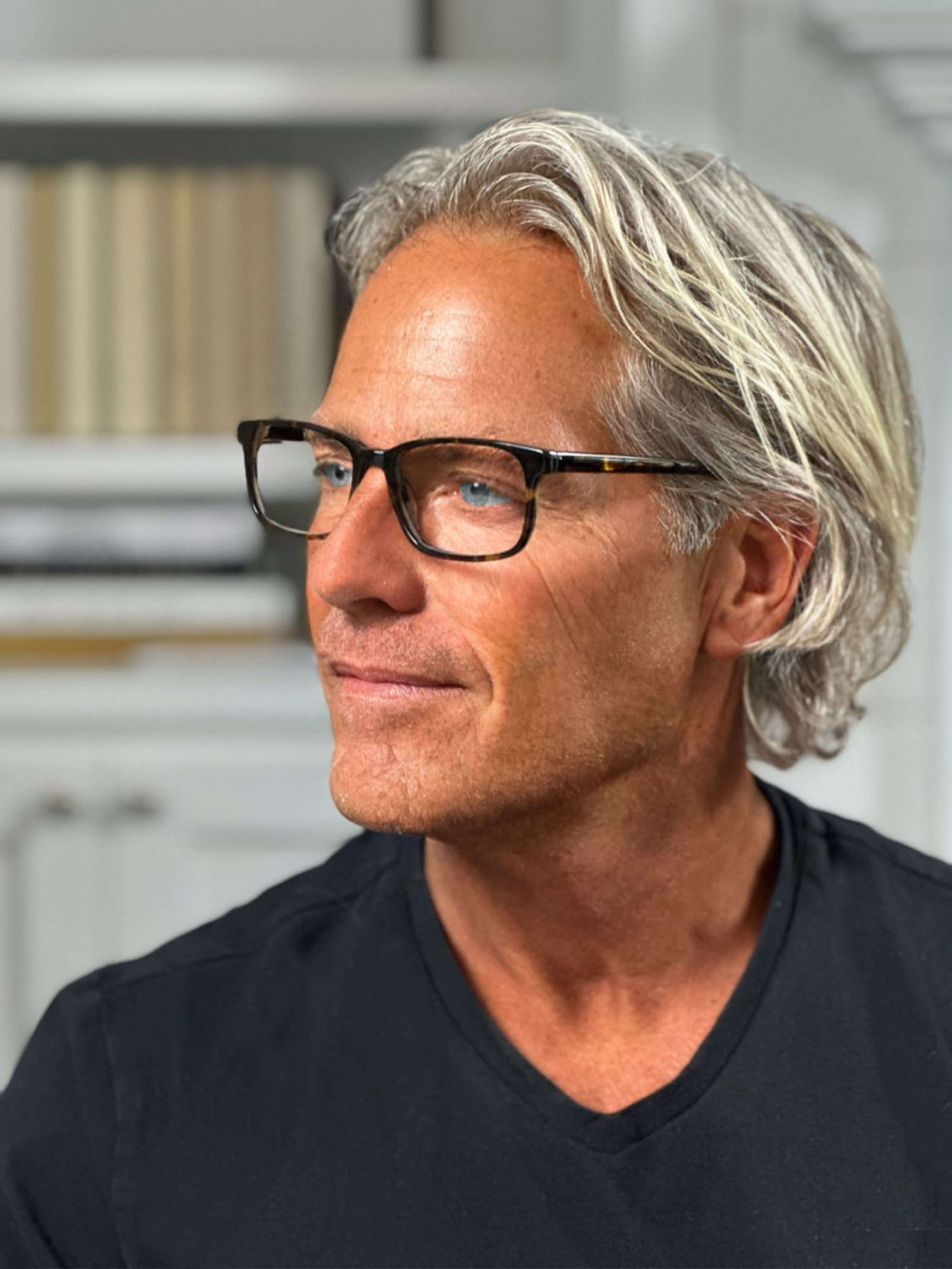 Man with gray hair and glasses wearing a black shirt indoors.
